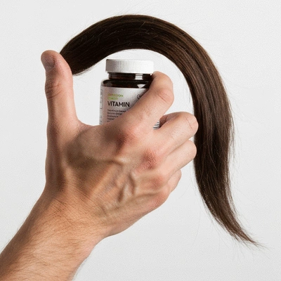 Close-up of a man's hand holding a vitamin bottle, with a healthy hair strand in the background, no text, no words, no typography, clean image
