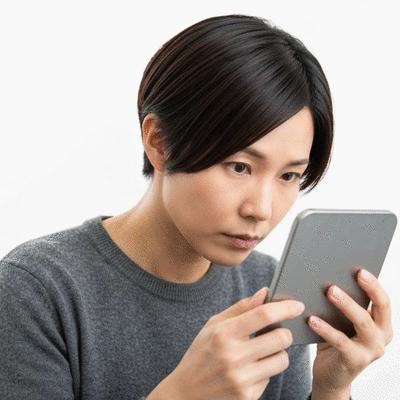 Person looking at their reflection in a small mirror, focusing on their hair, with a thoughtful expression. The background is clean and bright.